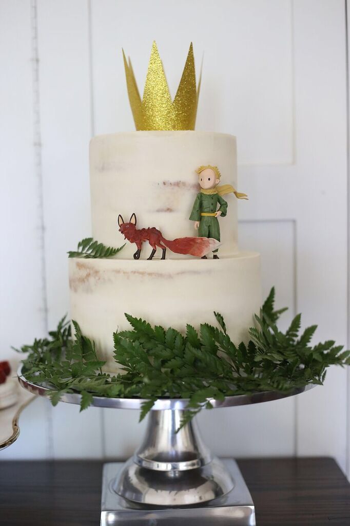 there is a white cake with green leaves on it and a gold crown on top