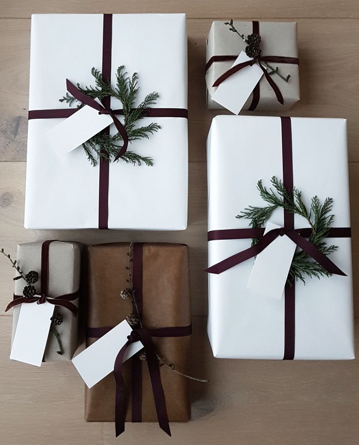 four wrapped presents with brown ribbon and pine tree decoration on them sitting on a wooden surface