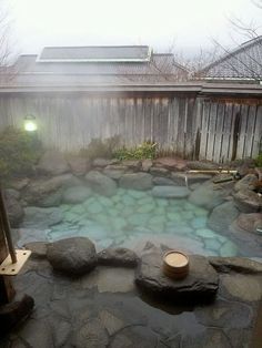 an outdoor hot tub in the middle of a yard with rocks and water surrounding it