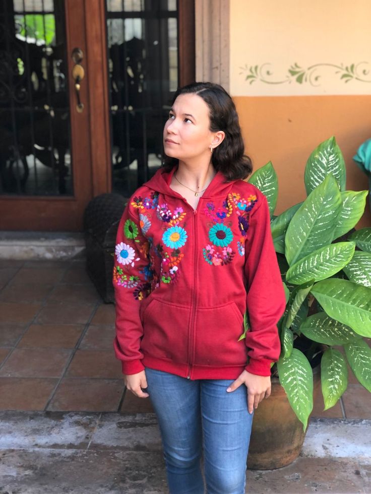 a woman standing in front of a door wearing a red jacket with colorful flowers on it