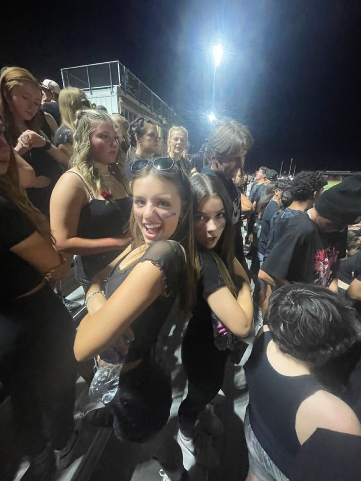 two young women standing next to each other in front of a group of people at night