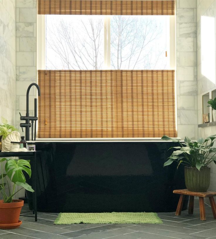 a black bath tub sitting next to a window covered in bamboo blinds