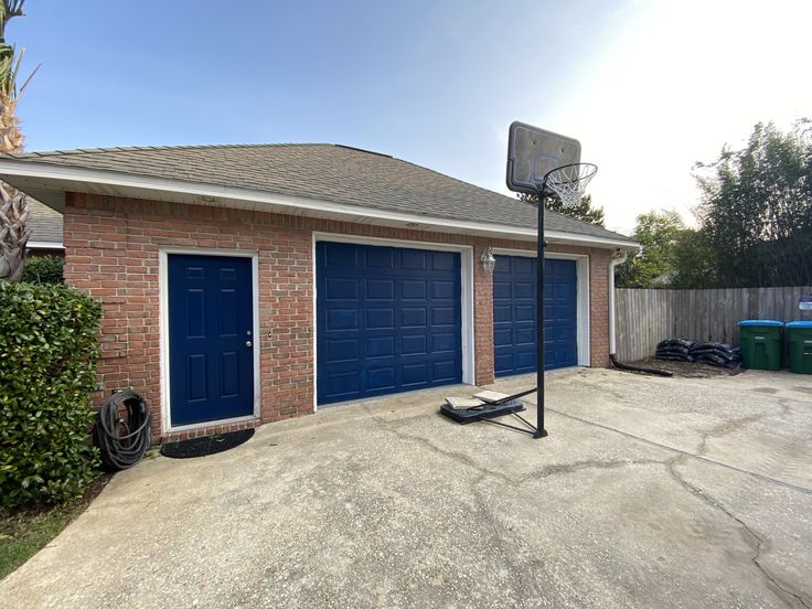 a basketball hoop in front of a garage with two blue doors and a basket on the driveway