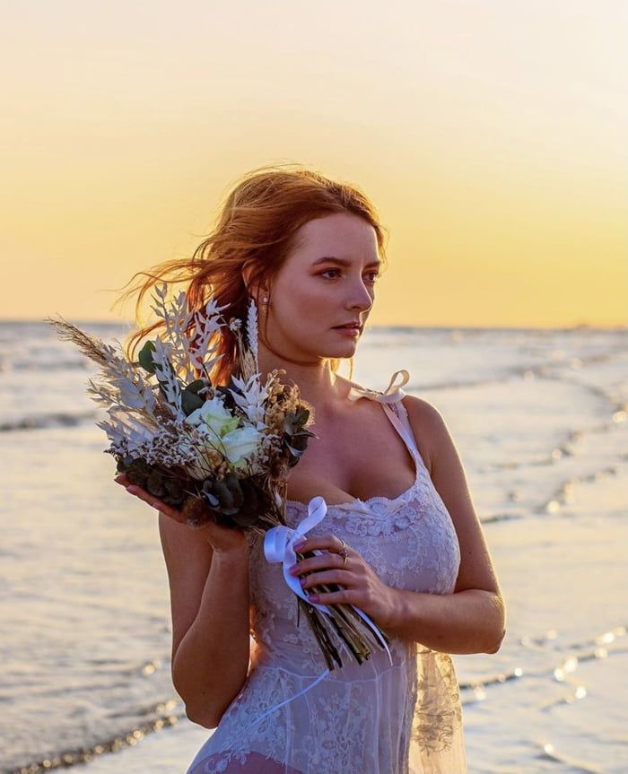 a woman standing on the beach with flowers in her hand