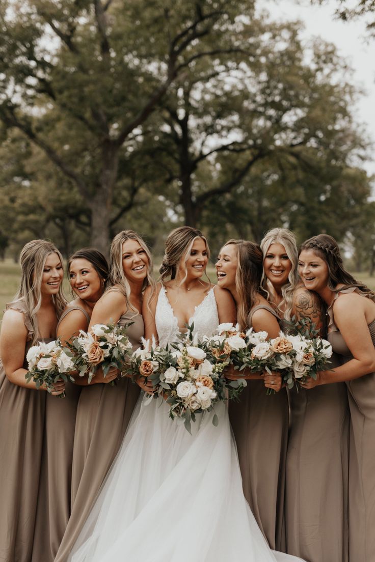 a group of women standing next to each other wearing dresses and holding bouquets in their hands