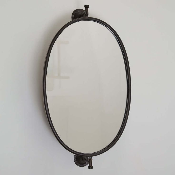 an oval mirror mounted on the wall above a faucet with a black handle