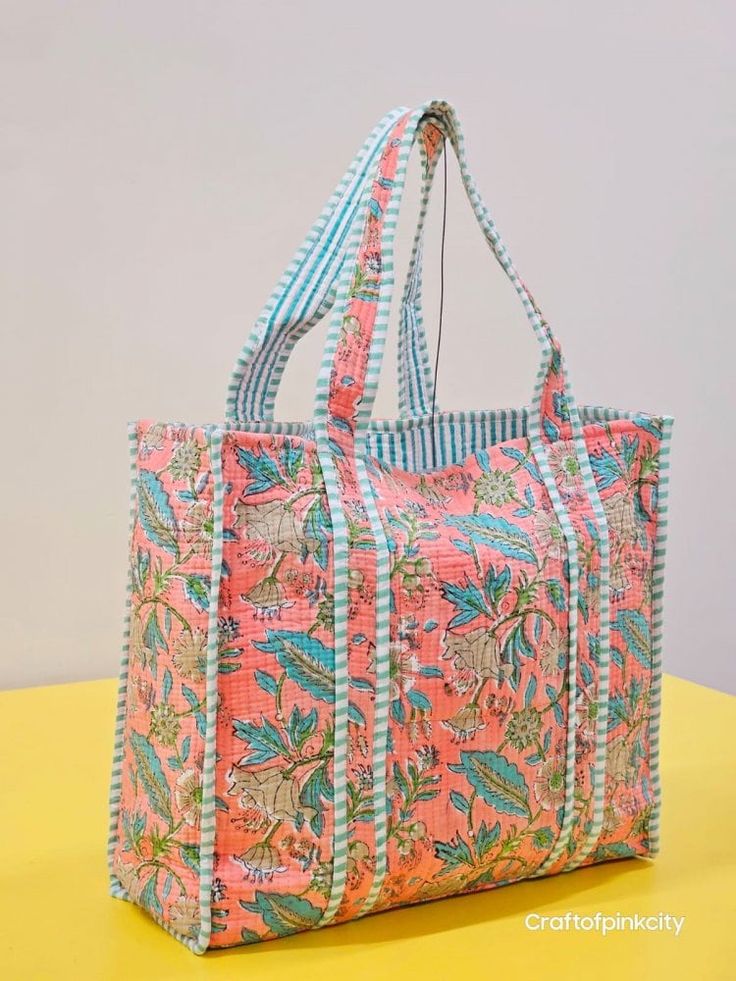 a pink and blue floral bag sitting on top of a yellow table next to a white wall