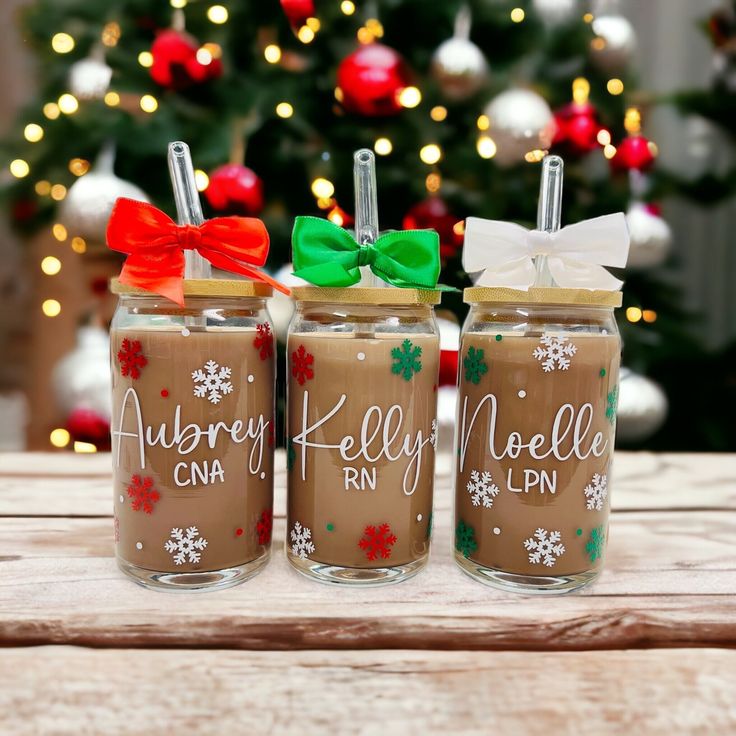 three decorated mason jars sitting on top of a wooden table next to a christmas tree