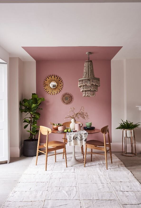 a dining room with pink walls and white rugs on the floor, chandelier hanging from the ceiling