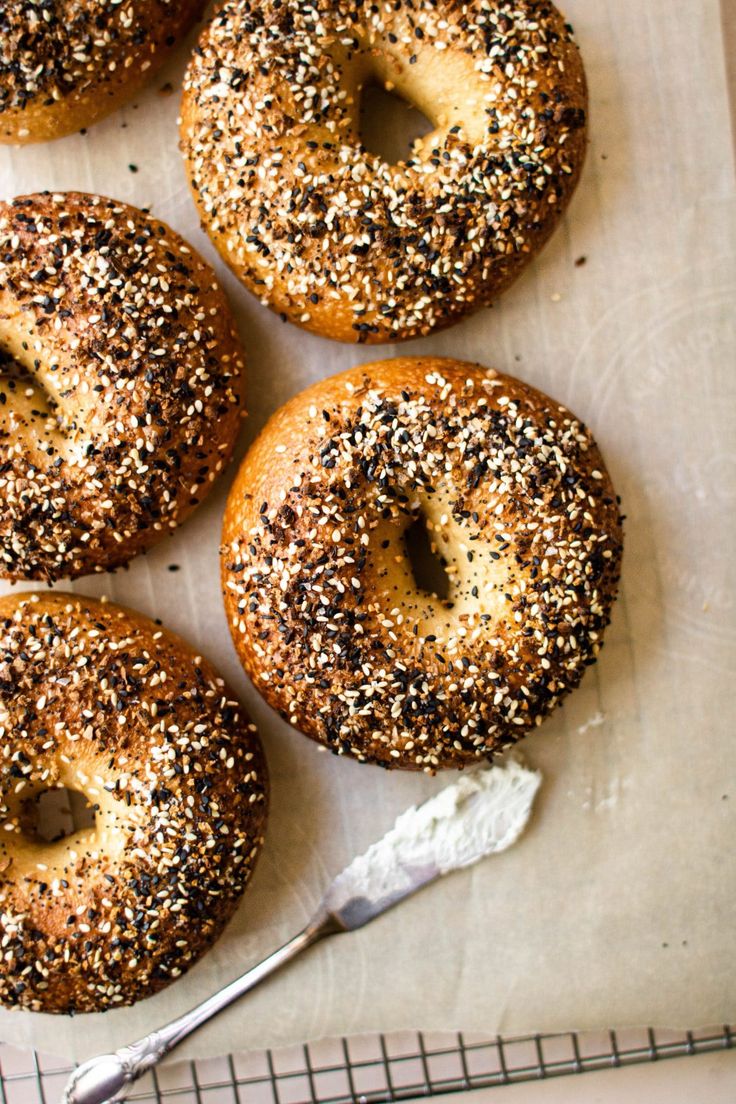 four bagels with sesame seeds are on a baking sheet, next to a spoon