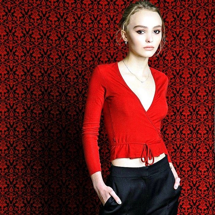 a woman standing in front of a red wall wearing black pants and a red top