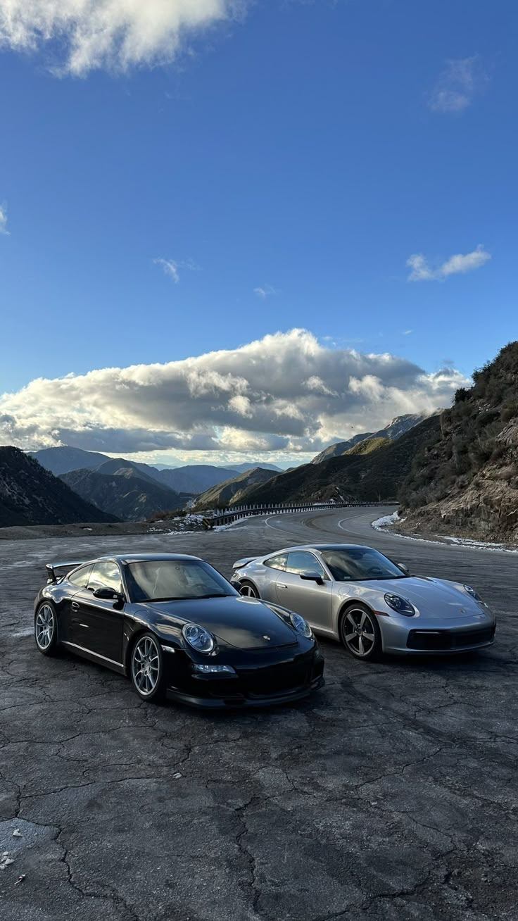 two sports cars parked in an empty parking lot with mountains in the backgroud