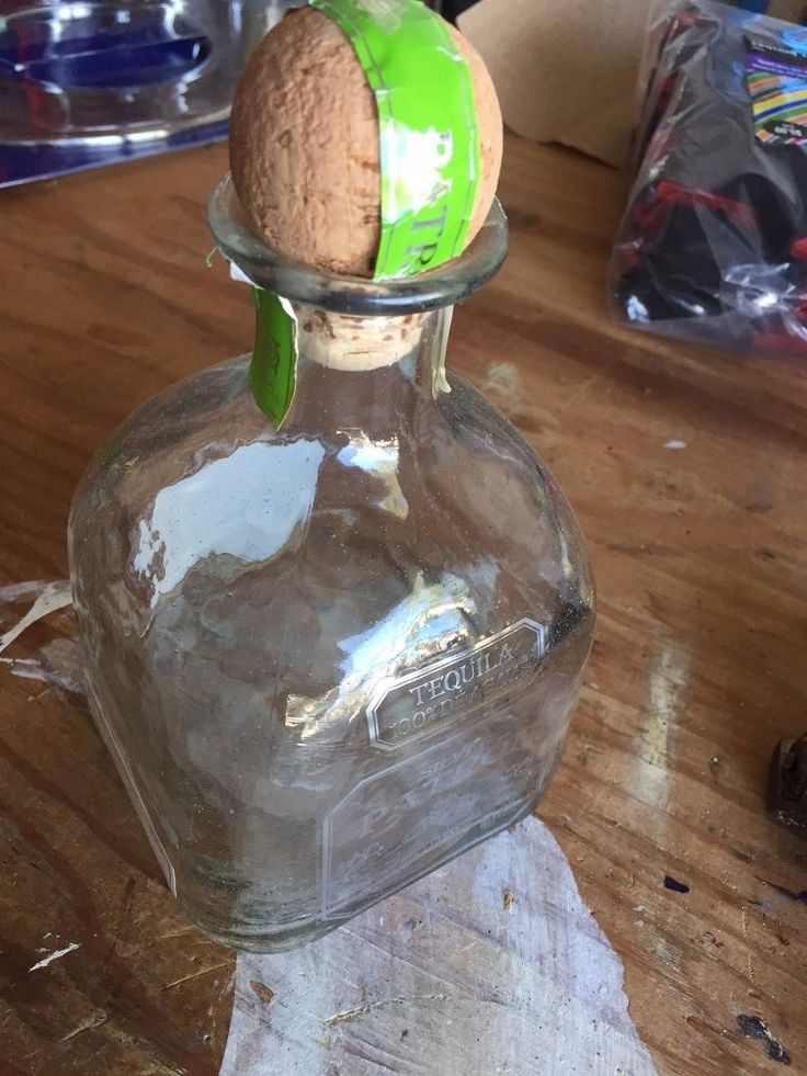 an empty glass bottle with a green apple in it on a wooden table next to other items