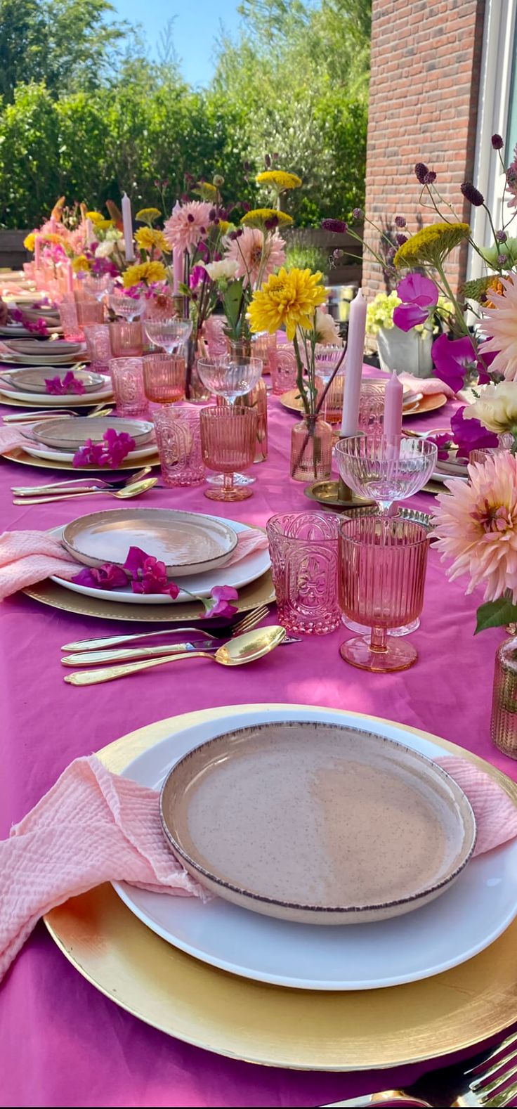 the table is set with pink and yellow plates, silverware, and flowers in vases