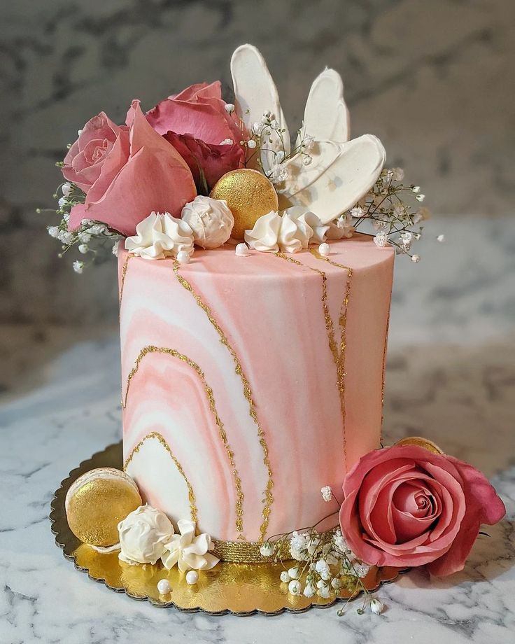 a pink and gold cake with flowers on it sitting on a marble countertop next to a rose