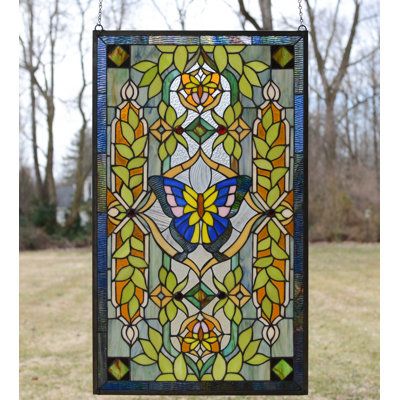 a stained glass window hanging on a pole in front of some grass and trees with no leaves