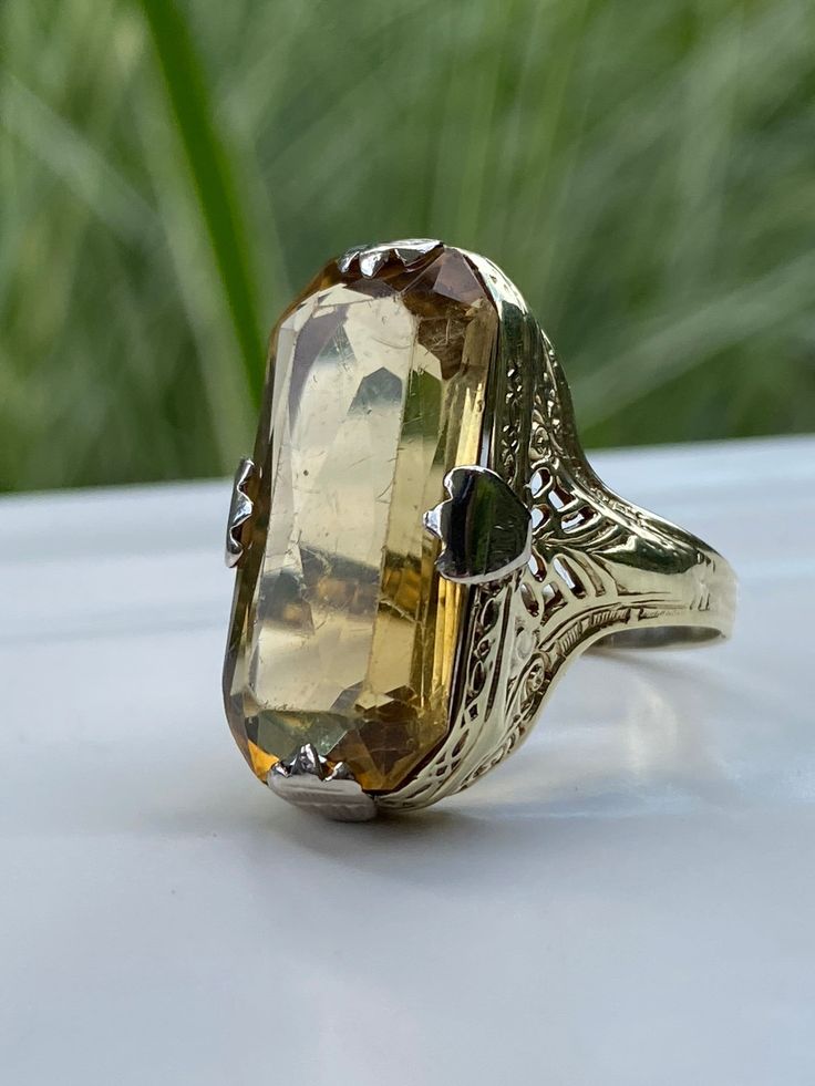 This is a lovely vintage Topaz cocktail ring, and what a darlin' she is. An 18k yellow gold band/setting with thick white gold prongs. The band features very organic, art nouveau-ish detailing. The Topaz is a smokey goldish color, which pairs beautifully with the colors in the band. Oh, that big ol' Topaz is 22 x 11mm. KAPOW! Please view the video for minor surface scratches to the topaz that are visible when viewing closely at certain angles. Not exceptionally noticeable. Details: Metal Purity Luxury Yellow Gold Topaz Ring In Art Deco Style, Luxury Vintage Topaz Ring Collectible, Vintage Luxury Topaz Ring Collectible, Luxury Yellow Gold Topaz Ring, Luxury Unique Yellow Gold Topaz Ring, Art Nouveau Gold Ring With Gemstone, Elegant Gold Topaz Ring With Polished Finish, Yellow Gold Art Nouveau Jewelry For Anniversary, Victorian Topaz Jewelry For Formal Occasions