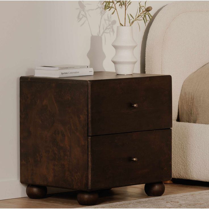 a nightstand with two drawers in front of a bed