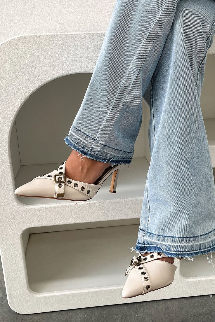 a woman's feet wearing white shoes and jeans sitting on top of a shelf