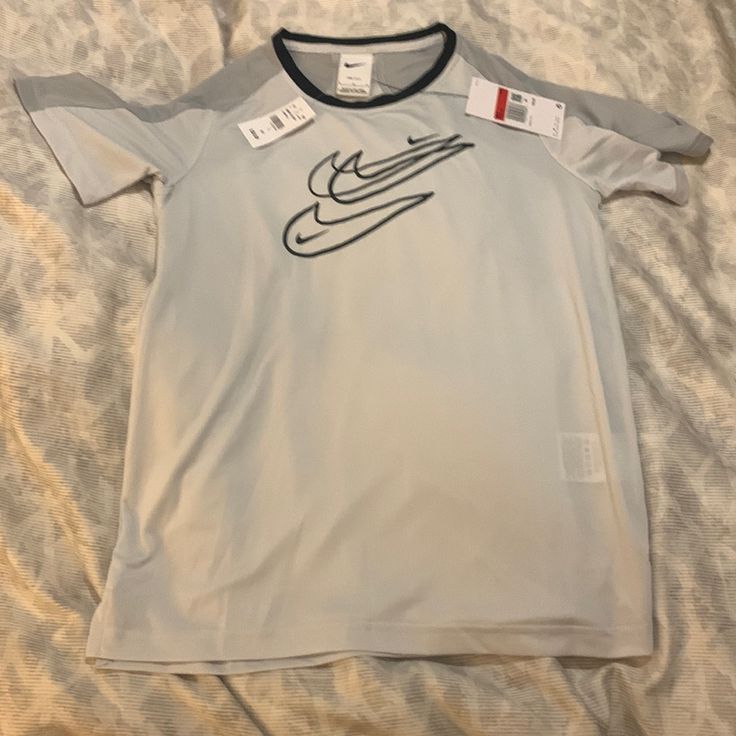 This Lightweight T-Shirt Is Light Gray With Dark Gray On The Shoulders. The Nike Swish Design Is In The Front. Gray Short Sleeve Sports Top, Nike Gray Sports T-shirt, White Moisture-wicking Short Sleeve Top, Nike Moisture-wicking Crew Neck Tops, Graphic Tee With Crew Neck For Sports, Nike Gray T-shirt With Logo Print, Nike Graphic Tee With Crew Neck, Nike Graphic Tee Crew Neck Shirt, Nike Short Sleeve Pre-shrunk Tops