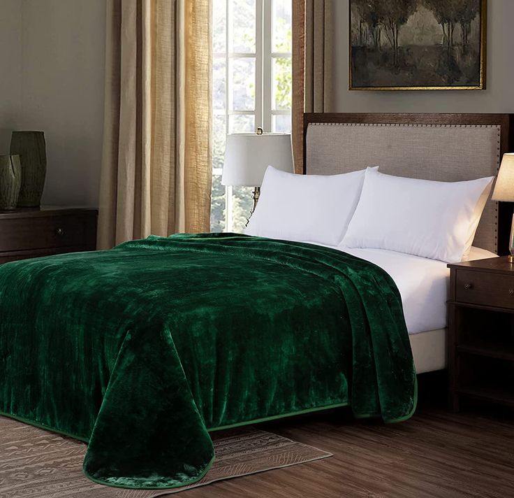 a large green blanket on top of a bed next to a night stand with two lamps