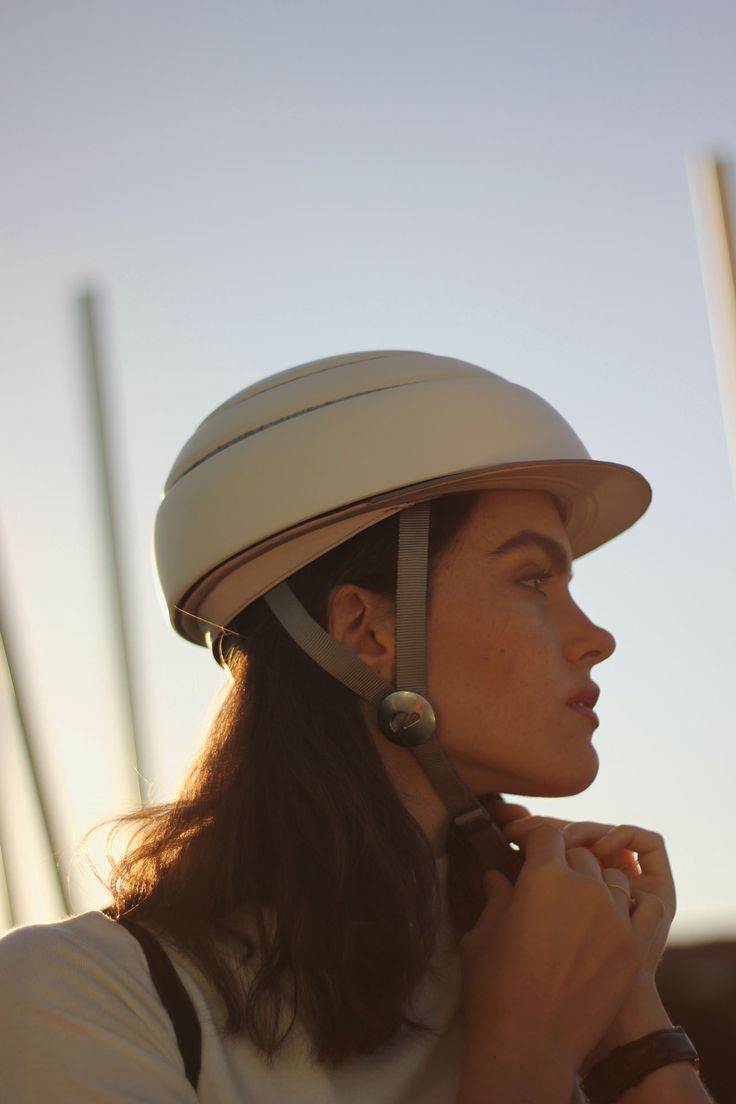 a woman wearing a white helmet and holding her hand to her ear while standing in the sun