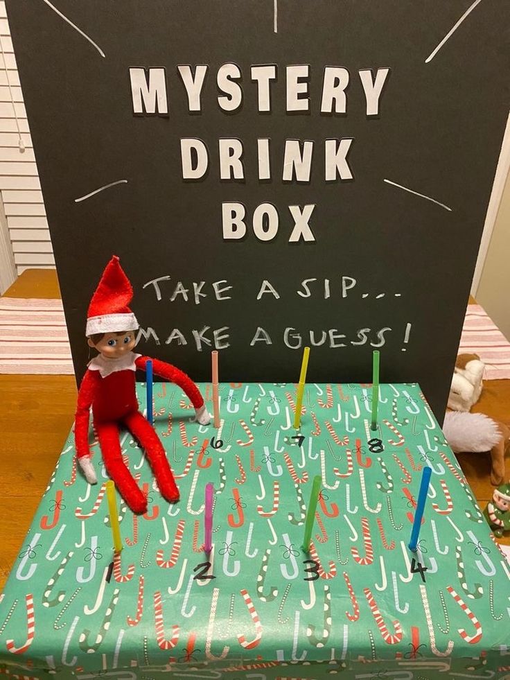 an elf sitting on top of a green box with candles in front of it that says mystery drink box