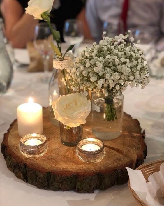 flowers and candles are placed in vases on a wood slice at a wedding reception