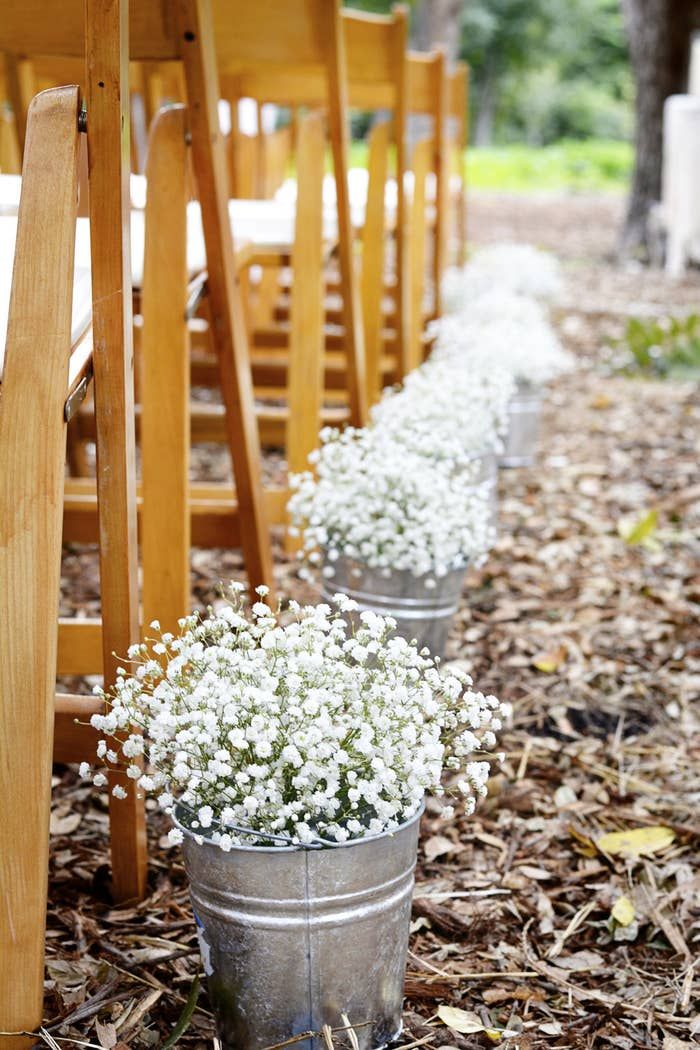 three buckets filled with baby's breath sitting on the ground next to wooden chairs