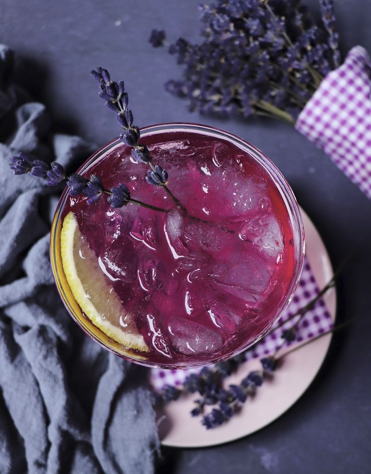 a purple drink with lavender sprigs on the rim next to a cloth and napkin