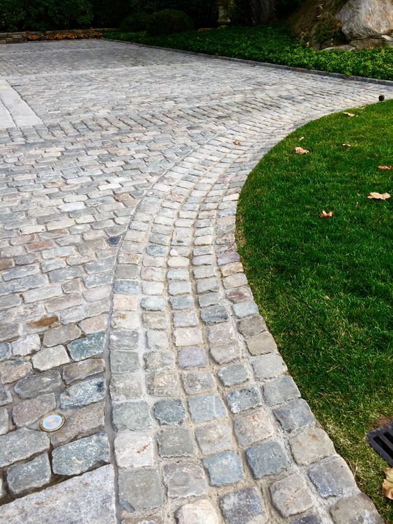 an empty bench sitting on the side of a brick road next to a grassy area