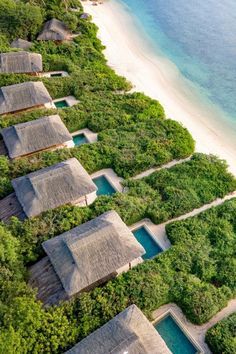 an aerial view of some huts on the beach with water and trees in the background