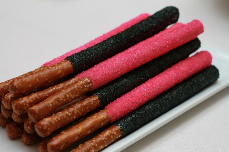 four different colored sticks are on a white plate with pink and black sugar coatings