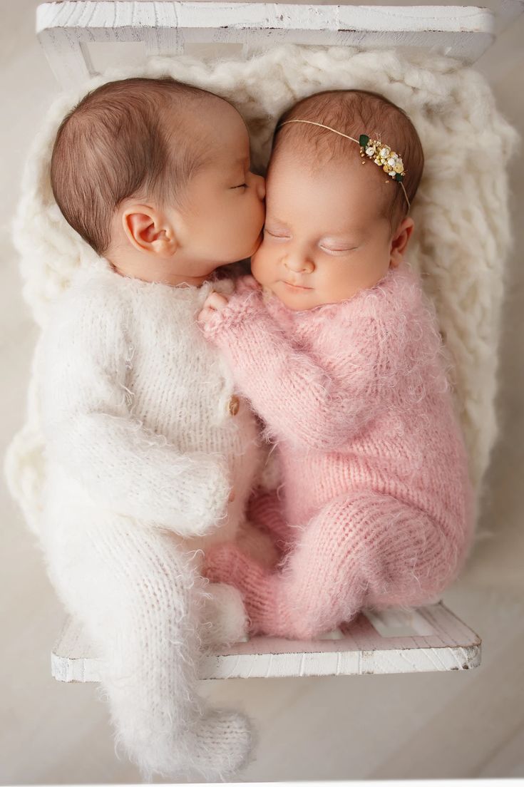 two newborn babies are cuddling in a white box with their heads touching each other