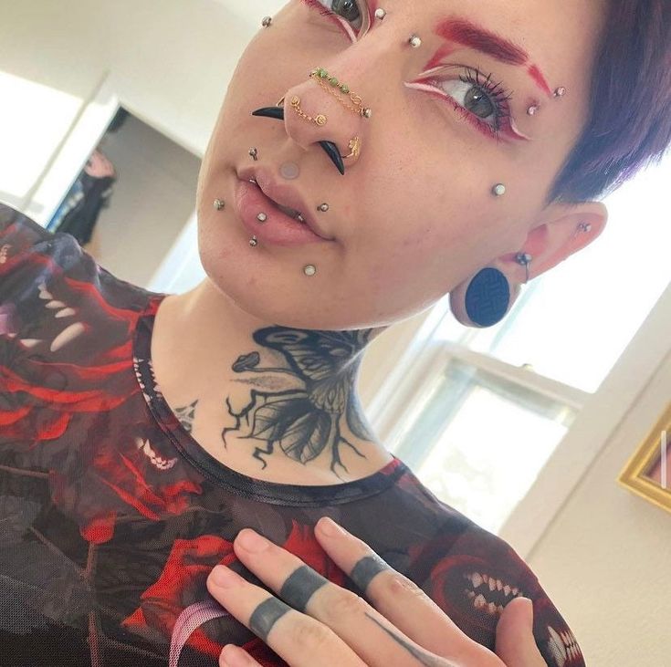 a woman with tattoos and piercings on her face is holding up her hand to the camera