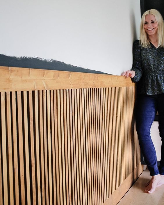 a woman standing next to a wooden wall with her hands on the top of it