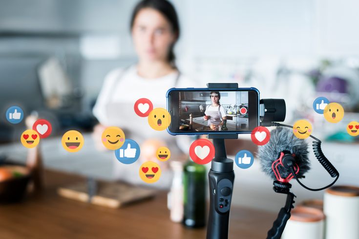 a woman is recording the video on her cell phone with emoticions surrounding her