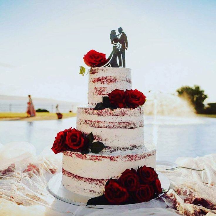 a wedding cake with red roses on the table