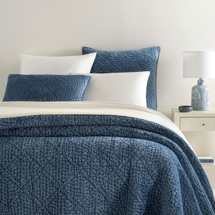 a bed with blue bedspread and white pillows on it in front of a night stand