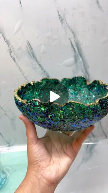 a hand holding a green and blue bowl on top of a marble counter next to a sink