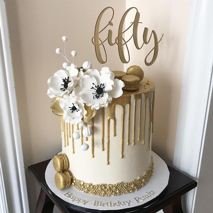 a white and gold birthday cake with flowers on the top is sitting on a table