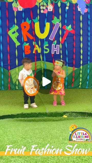 two children are standing in front of a colorful banner with the words fruit fashion show on it