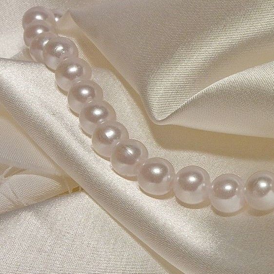 a close up of a white satin with pearls on the side and fabric in the background