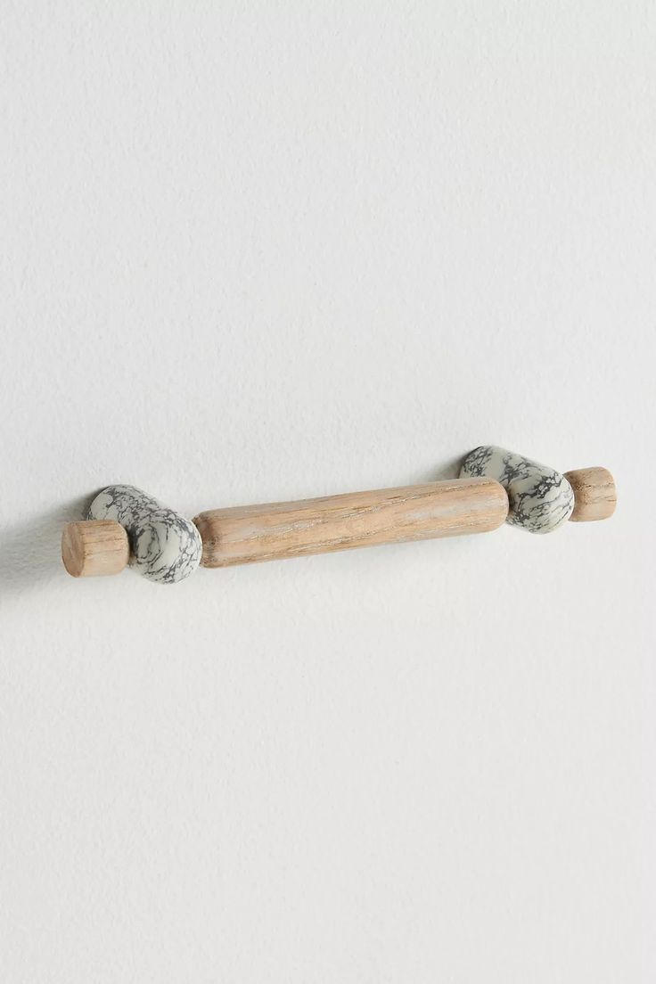 a white wall with two wooden pegs on the top and one wood stick in the middle