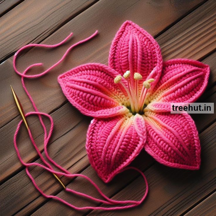 a pink crocheted flower sitting on top of a wooden table next to a pair of scissors