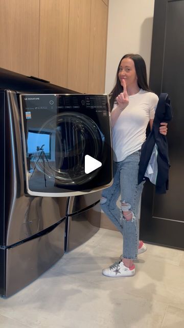 a woman standing in front of a washing machine with the door open and her thumb up