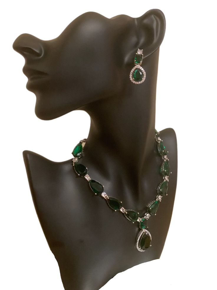 Experience the beauty and elegance of our CZ American Diamond Necklace. Adorned with stunning green stones, this necklace is perfect for any occasion, whether it's a wedding, party, or a gift for someone special. Pair it with outfits like sarees, gowns, or lehengas to complete your look. This jewellery set includes a necklace and matching earrings. Jewellery Care- Keep the jewellery dry, avoid contact with perfumes and water. Formal Bridal Necklace With Emerald Gemstones, Dazzling Green Emerald Necklace, Elegant Kundan Emerald Necklace For Festive Occasions, Green Emerald Kundan Necklace As A Gift, Elegant Emerald Kundan Necklace For Festive Occasions, Green Emerald Kundan Necklace For Gift, Green Jewelry Sets With Stones For Party, Green Stone Jewelry For Formal Occasions, Dazzling Green Emerald Necklace For Formal Occasions