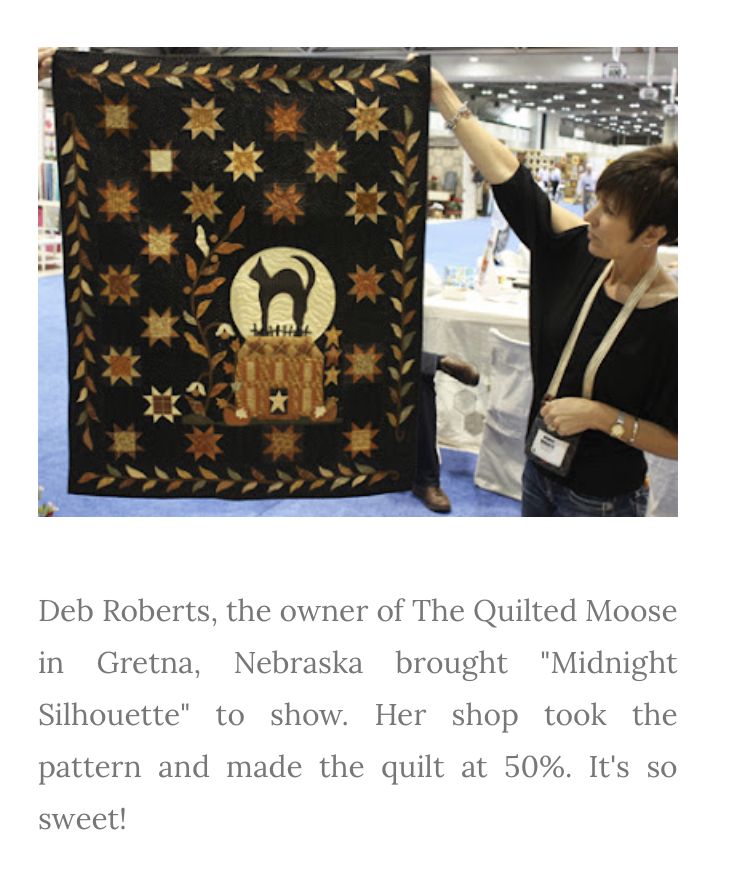 a woman is holding up a quilt on display