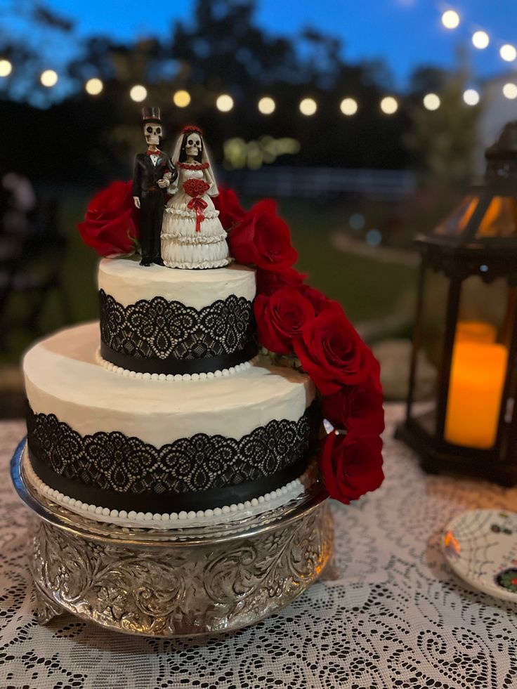 a wedding cake with red roses on top and a couple figurine on top