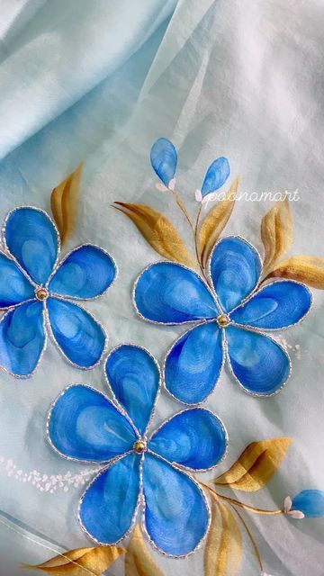 two blue flowers with gold leaves are on a white fabric background, and the image is made up of glass beads